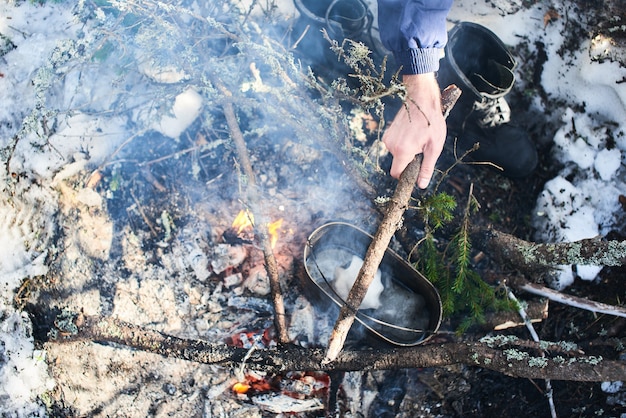 Hand schmilzt den Schnee auf dem Feuer in einem Topf