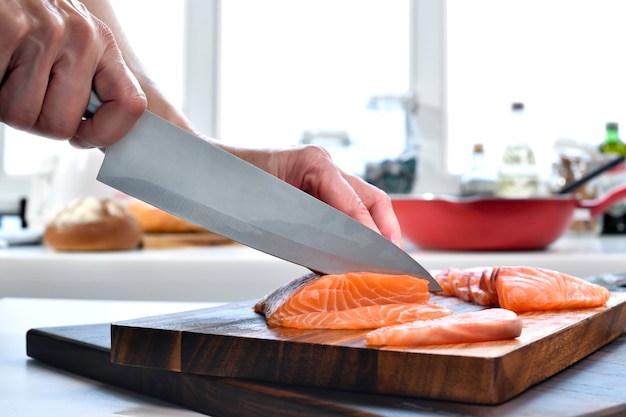 Hand schneiden frische rohe Lachsfiletsteaks auf einem Schneidebrett in der Küche