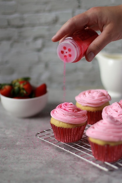 Hand streut rosa Streusel auf Muffins mit rosa Buttercreme-Zuckerguss darauf