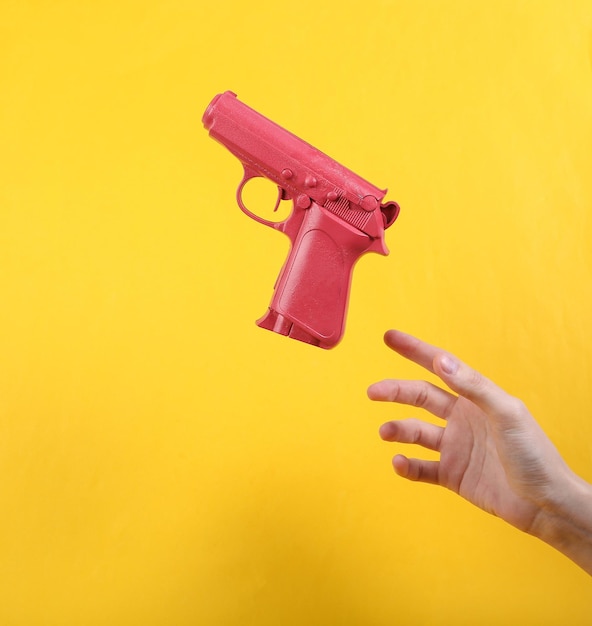 Hand und schwebende rosa Waffe auf gelbem Hintergrund Minimalistisches Stillleben Konzeptkunst Videospiel