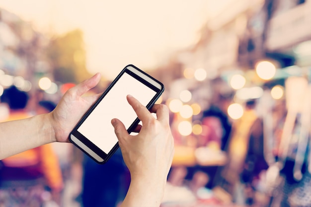 Hand unter Verwendung des Smartphone und der unscharfen Menge von den Leuten, die durch eine Stadtstraße gehen. Weinlese getontes Foto.