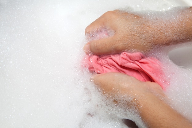 Hand waschende Kleidung mit Blase auf weißem Becken.