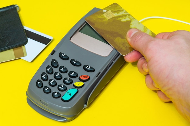 Hand wendet Bankkarte an Geldterminal zur Zahlung auf gelbem Schreibtisch an, Ansicht von oben