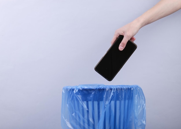 Hand wirft Smartphone mit Paket auf grauem Hintergrund in Mülleimer