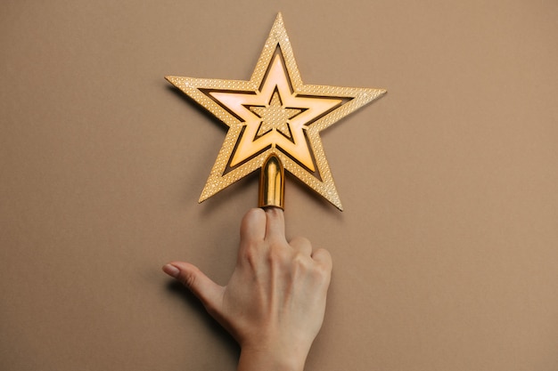 Hand zeigt Mittelfinger mit goldenem Stern auf braun verziert