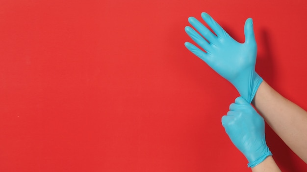 Hand zieht blaue Latexhandschuhe oder chirurgische Handschuhe auf rotem Hintergrund.