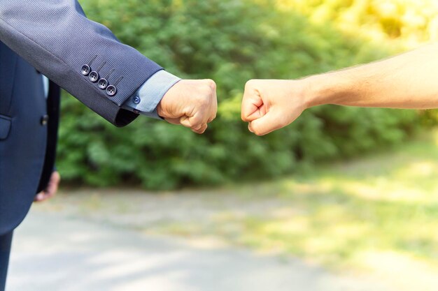 Handbewegungen. Fauststoß als beliebter Gruß zwischen besten Freunden. Händedruck gegen grünen Park Hintergrund im Sommer. Stoppen Sie die Ausbreitung des Coronavirus. Die Faustbegrüßung ist eine Alternative zum Händedruck.