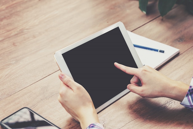 Handfrau, die Tablet-Computer auf Holztisch mit der Weinlese getont verwendet.