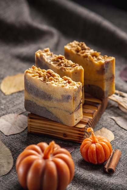 Handgefertigte duftende natürliche Seife und Kürbisformige Kerzen auf dunklem Hintergrund mit gelben trockenen Blättern, um eine gemütliche Atmosphäre zu schaffen Schöne Herbstpostkarte