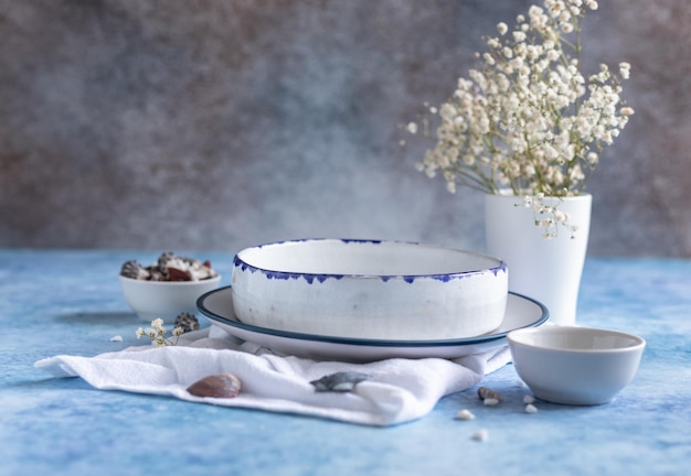 Handgefertigte weiße Keramikteller mit blauem Streifen am Rand getrocknete Blumen und leere Muscheln