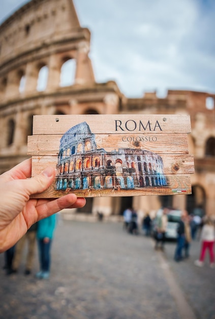 Handgehaltene Postkarte mit Colosseum-Druck in der Straße von Rom