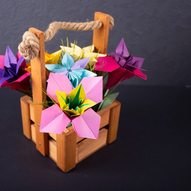 Handgemachte farbige Papierblumen Origami-Straußpapier-Bastelkunst in einem Korb mit Gras im Studio auf farbigem Hintergrundmakro