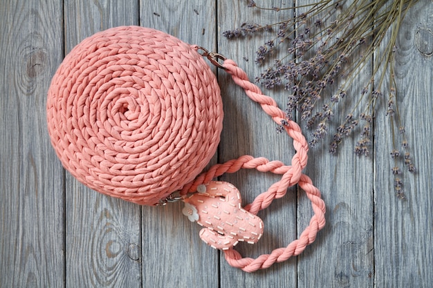 Handgemachte gehäkelte rosa Tasche mit langem Griff, Beschlägen und dekorativ genähtem Kaktus auf dem Holztisch mit Lavendelblüten.