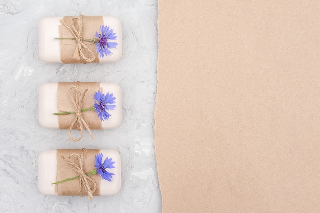 Foto handgemachte natürliche seife set grenze mit bastelpapier, geißel und blauen kornblumen auf grauem stein hintergrundansicht flach gelegt kopieren raum verziert