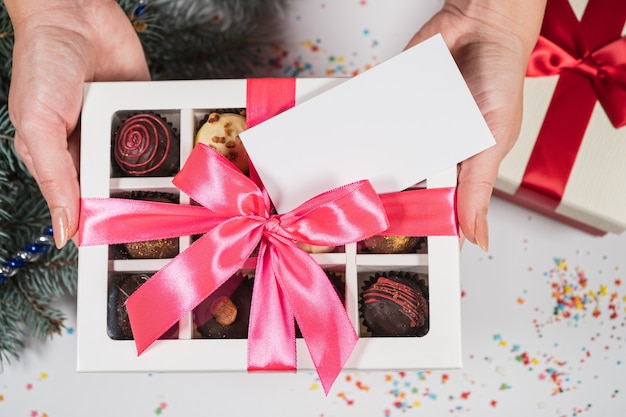 Handgemachte Schokoladentrüffelbonbons in den Händen einer Frau auf einem Weihnachtshintergrund mit Visitenkarte