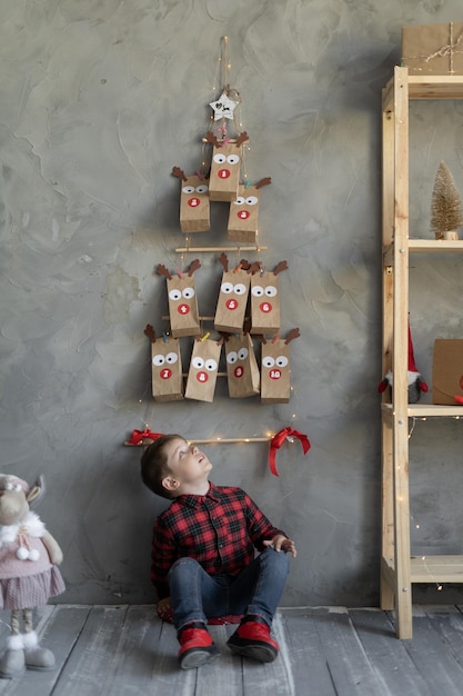 Foto handgemachter adventskalender in einer handwerkstasche, der an der wand hängt. junge sitzt auf dem boden und schaut auf weihnachten. horizontale position konzept der weihnachtstraditionen