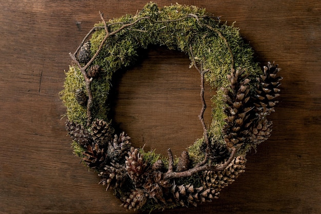 Handgemachter DIY-Handwerks-Weihnachtsfeiertagskranz mit natürlichem trendigem Waldmoos und Zapfen auf hölzernem Hintergrund.