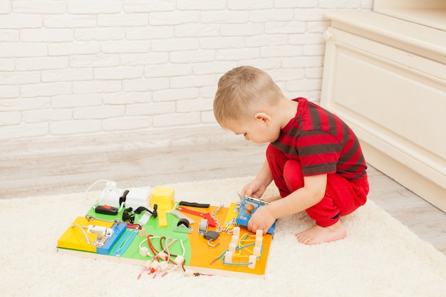 Handgemachtes DIY sensorisches Kinderspielzeug, dreijähriger Junge spielt mit beschäftigtem Brett