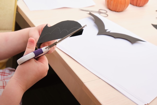 Foto handgemachtes halloween-dekor. kind schneidet eine fledermaus aus schwarzem papier