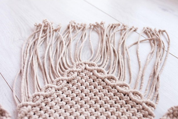 Handgemachtes Makramee-Muster aus nächster Nähe Makramee-Flechten und Baumwollfäden auf Holztisch Weibliches Hobby ECO-freundliches modernes Stricken DIY natürliches Dekorationskonzept