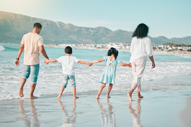 Handhaltende Familie geht am Strand spazieren und Blick von hinten auf Meereswellen, Sommer und Verbundenheit in der Natur, Eltern, Kinder und Menschen im Freien im Urlaub, Freiheit und Reisen, Vertrauen und Liebe in Mexiko