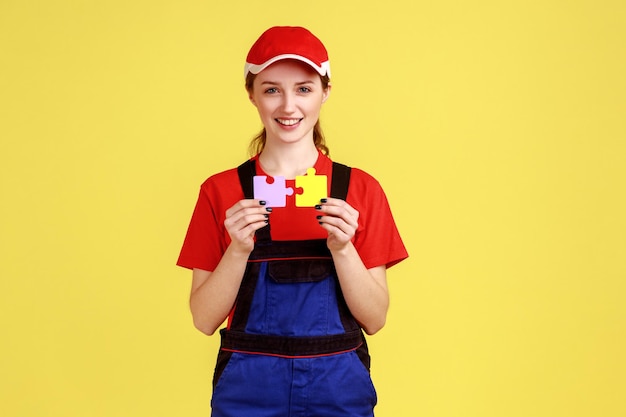 Handliche Frau, die zwei Puzzleteile hält und mit glücklichem Gesichtsausdruck in die Kamera blickt