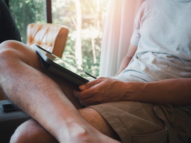 Handmann mit digitaler Tablette. Ein junger Mensch, ein Mann in lässigem grauem Hemd und Shorts, der zu Hause sitzt und mit Technologie interagiert. Entspannungsgeschäftsmann, der online an jedem Konzept arbeitet.