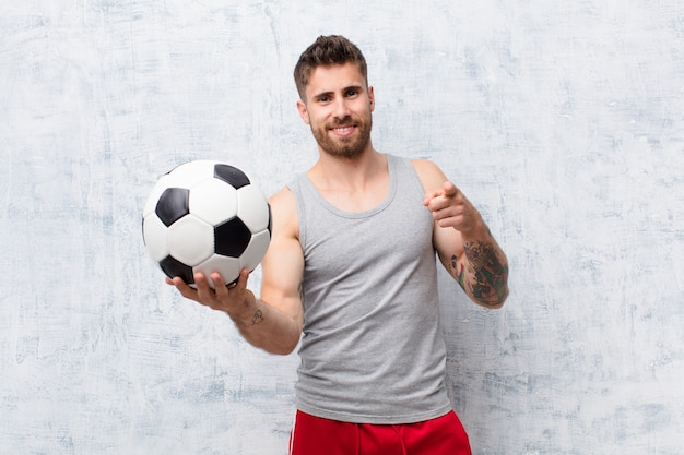 Handosme jovem homem contra a parede com uma bola de futebol. conceito de esporte