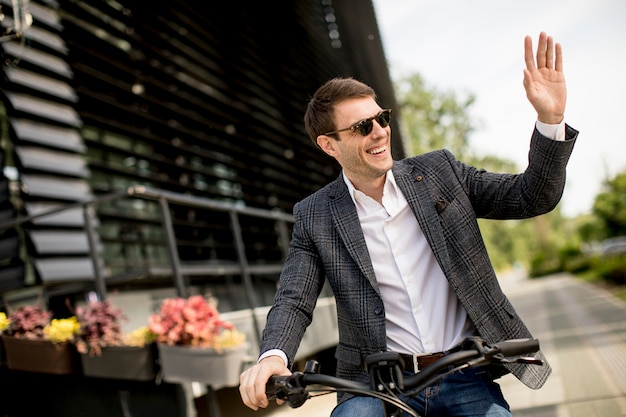 Handosme joven empresario en la bicicleta eléctrica en la calle