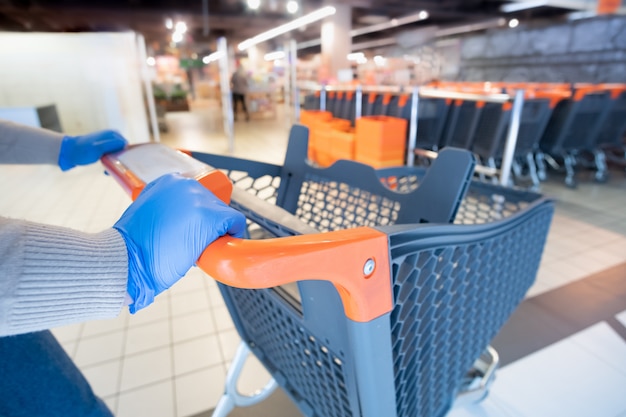 Hands in Glives mit einem Einkaufswagen in einem Supermarkt.