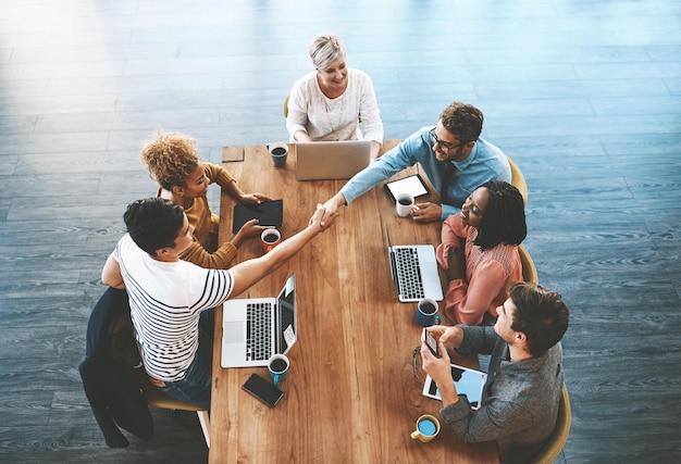Handschlag oben und Geschäftsleute in einem Meeting für ein Deal-Onboarding und Willkommensgrüße. Fröhliches Vorstellungsgespräch und Unternehmensmitarbeiter, die sich in der Gruppendiskussion als Dankeschön für ihre Unterstützung oder Partnerschaft die Hand schütteln
