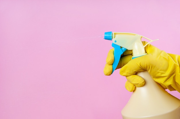 Handschuh-Hand sprüht aus einer Sprühflasche auf einem rosa Hintergrund, kopieren Raum, verspotten