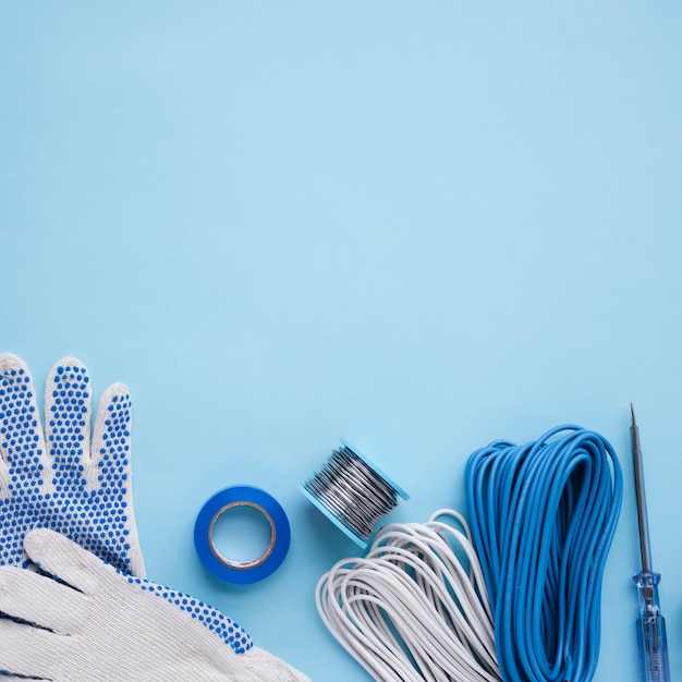 Handschuhe; Band; metallische Drahtspule; Draht und Tester auf blauer Oberfläche