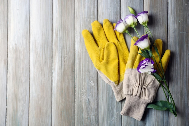 Handschuhe des gelben Gärtners und empfindliche Blüte auf grauem hölzernem Hintergrund