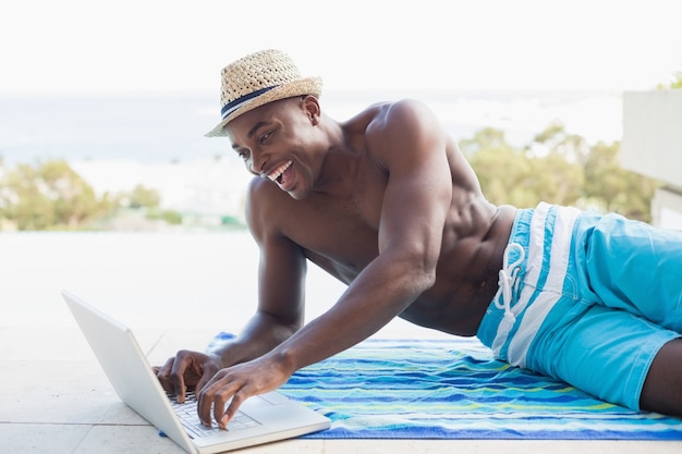 Handsome, homem sem camisa, usando laptop, ao lado da piscina