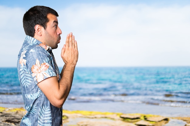 Handsome Mann mit Blumen-Shirt flehend am Strand