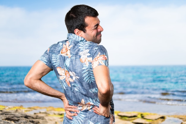 Handsome Mann mit Blumenhemd mit Rückenschmerzen am Strand