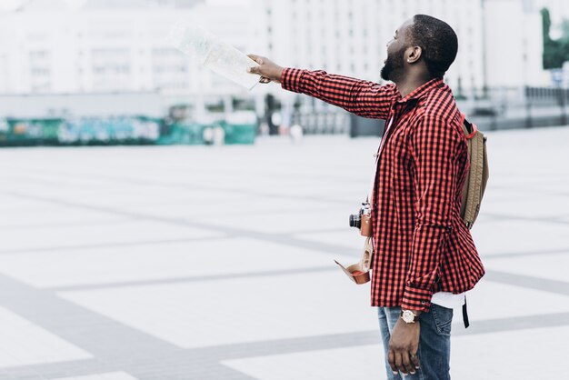 Handsome und glücklich Afro American Tourist mit alten Kamera und Karte in der modernen Stadt