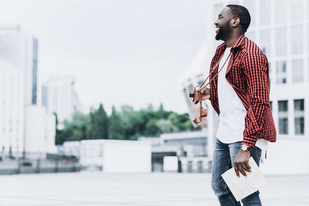 Handsome und glücklich Afro American Tourist mit alten Kamera und Karte in der modernen Stadt