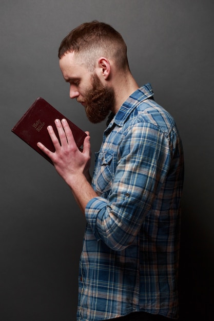 Handsone Mann, der über Bibel in einem dunklen Raum über grauer Beschaffenheit liest und betet