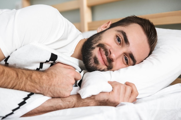 Handsonme lächelnder Mann, der auf einem Kissen im Bett schläft