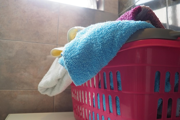 Handtücher im Wäschekorb Blaue und rosafarbene Frotteehandtücher aus Baumwolle werden in einen rosafarbenen Kunststoffkorb geworfen. Housekeeping Aufbewahrung und Trennung der Wäsche vor dem Waschen. Licht von oben durch offenes Fenster