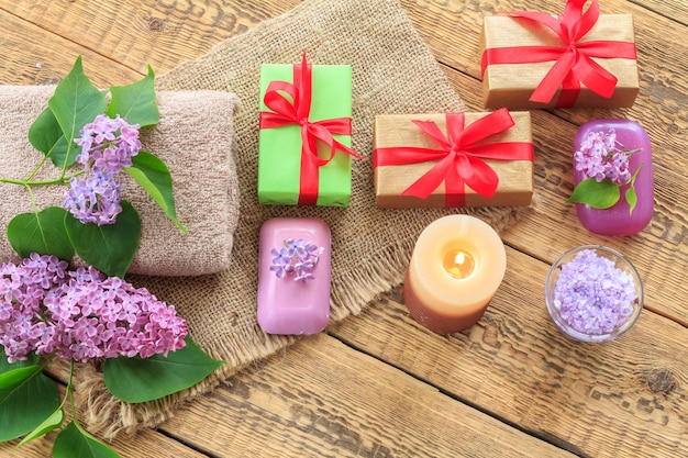 Handtücher Seifengeschenke Kerze und lila Blumen auf Holzhintergrund