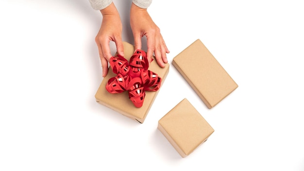 Handverpacken von Geschenken aus Kraftkarton mit einem roten Band auf weißem Hintergrund