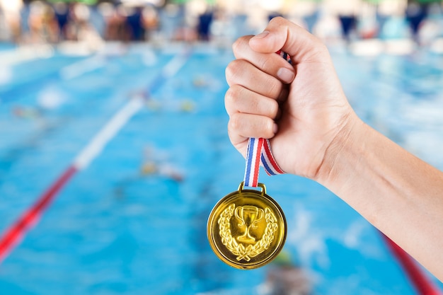 Handvoll asiatischen Mann mit Goldmedaille mit verschwommenen Hintergrund von Schwimmbad und Schwimmen Wettbewerb.