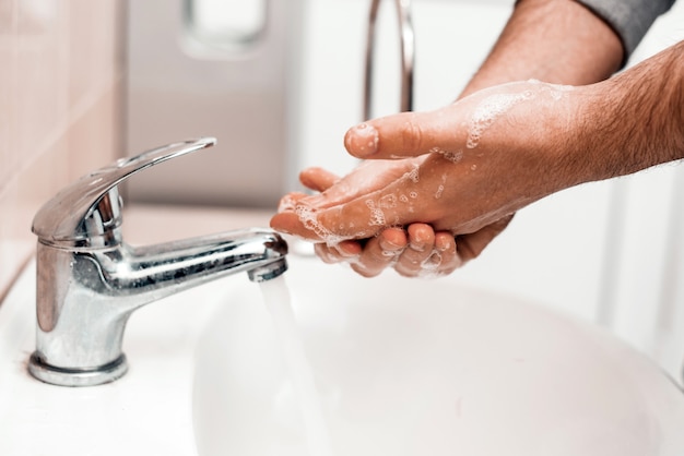 Handwäsche mit Seife in einem Waschbecken an einem öffentlichen Ort. Hygienekonzept. Hände waschen mit Seife unter dem Wasserhahn mit Wasser