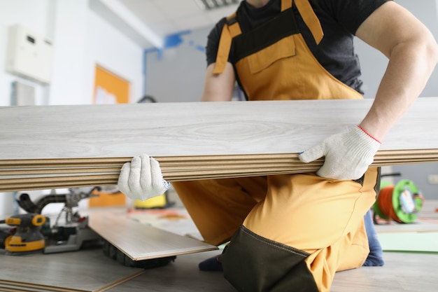 Handwerker, der Laminatbrett in den Händen hält, um den Boden in Nahaufnahme zu verlegen