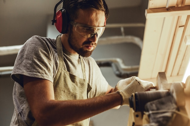 Handwerker, der mit Holz auf Bandschleifer arbeitet