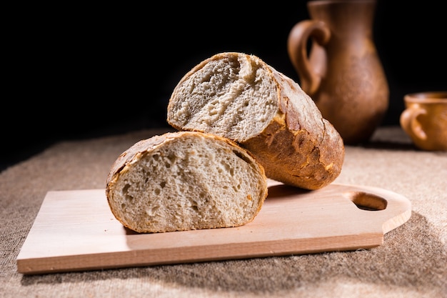 Handwerker gebackenes Vollkornbrot in zwei Hälften geteilt auf rustikalem Holzbrett auf Tisch mit Krug und Tasse