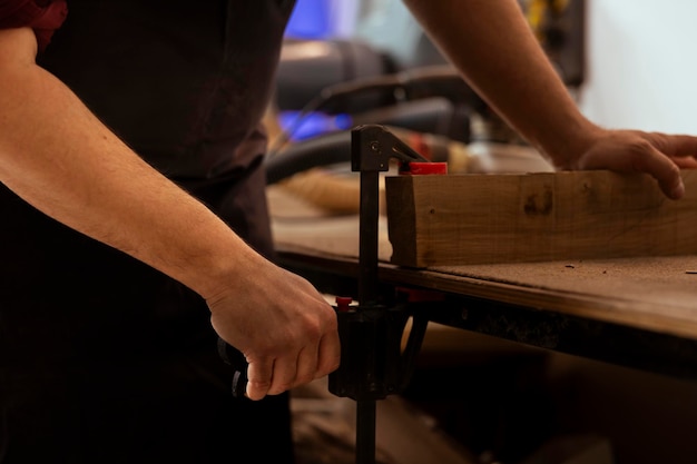 Foto handwerker in der tischlerkunst, der ein holzstück mit einem schraubwerkzeug festhält